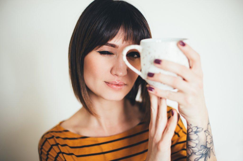 Young woman hipster with tatoo drinking tea or coffee on white background.