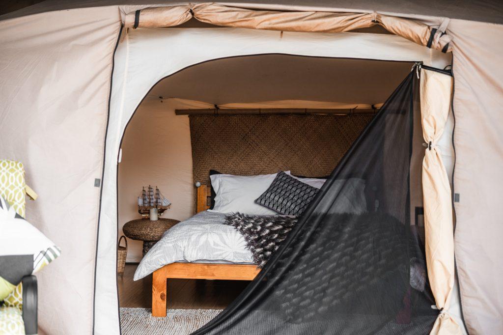 interior of a tent with a cozy bed mattress blanket and cushions wrapped in a mosquito net, tarawera